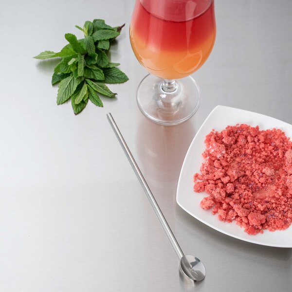 A stainless steel Barfly straw next to a plate of food and a glass of liquid.