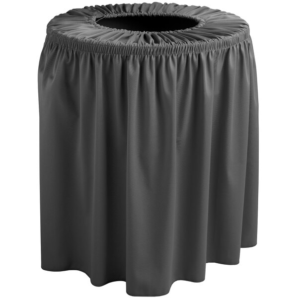 A black round trash can with a black ruffled cover on a grey table.