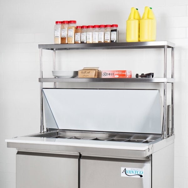 An Avantco stainless steel double deck overshelf on a counter above a stainless steel refrigerator.