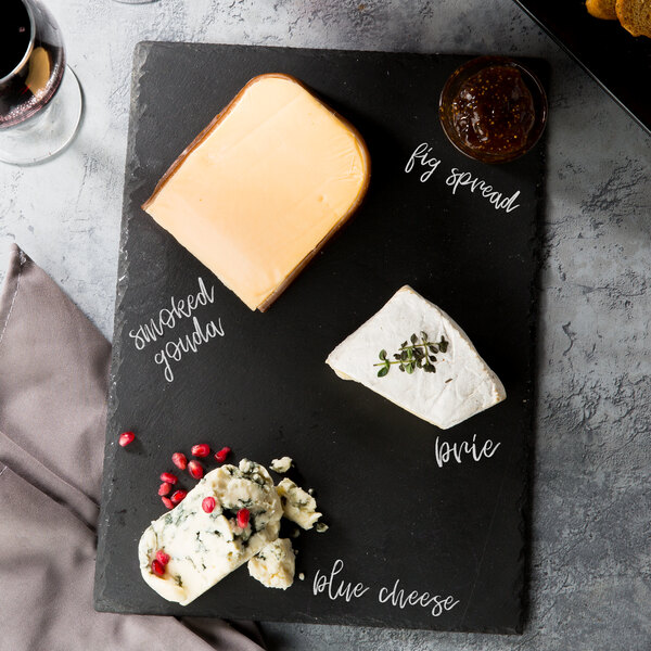 A rectangular black slate tray with cheese, wine, and crackers on it.