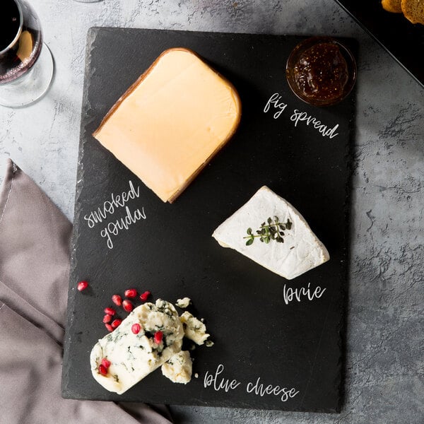 A black slate tray with pieces of cheese, wine, and crackers with a piece of blue cheese with pomegranate seeds on it.