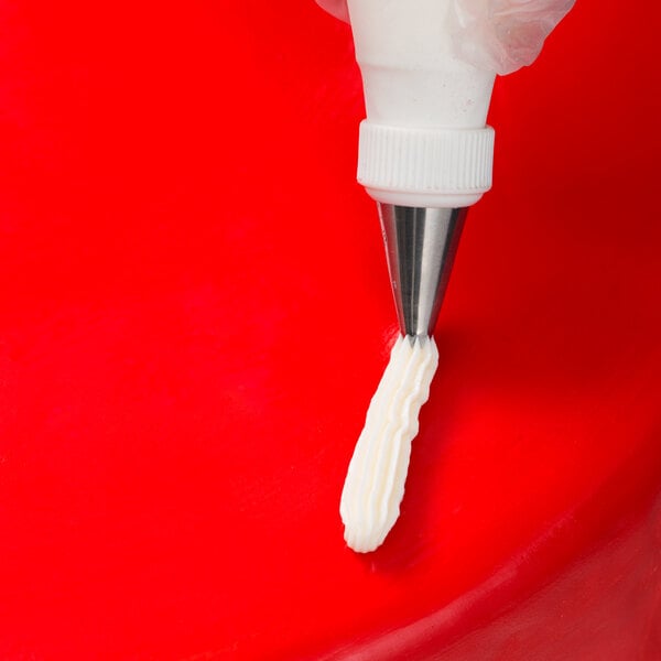 A person using an Ateco pastry bag with a ruffle piping tip to pipe white frosting.
