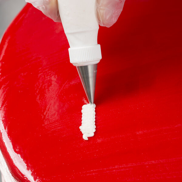 A hand using an Ateco Open Star piping tip to pipe white icing onto a cake.