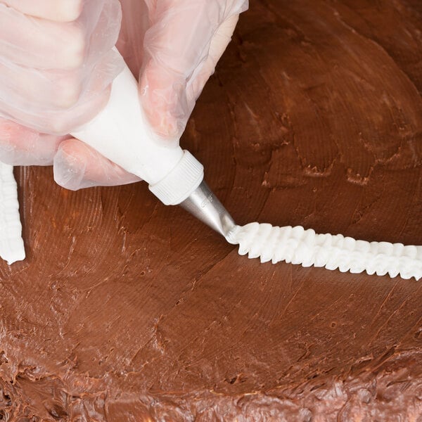A person using an Ateco curved petal piping tip to decorate a brown cake with frosting.