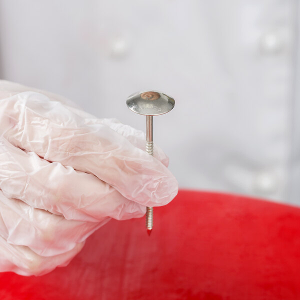A hand in gloves holding an Ateco stainless steel flower nail.