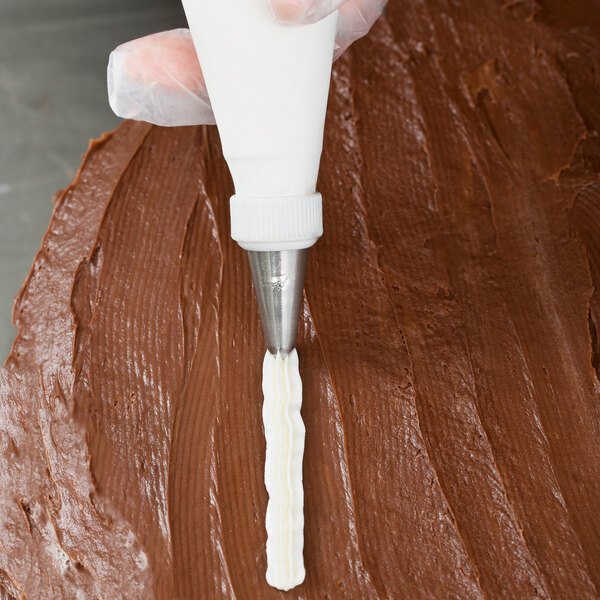 A person using an Ateco cross-top piping tip on a pastry bag to decorate a chocolate cake.