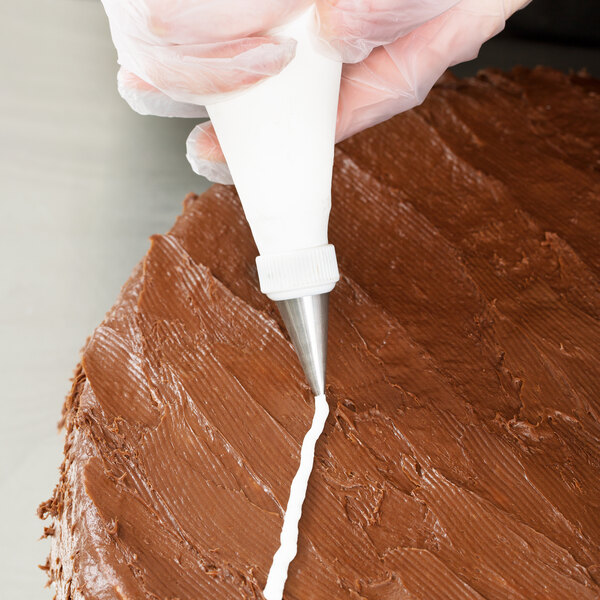 A person using an Ateco oval piping tip in a pastry bag to frost a chocolate cake.