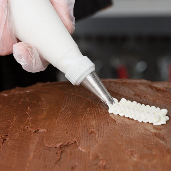 A person using an Ateco leaf piping tip to frost a brown cake with a pastry bag.