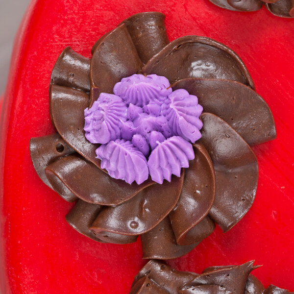 A close up of a chocolate cake with purple flowers piped using an Ateco 247 Russian piping tip.