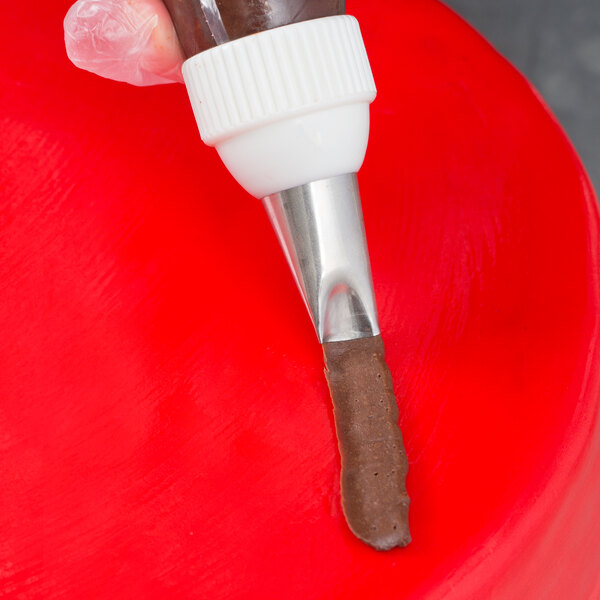 A hand holding a pastry bag with chocolate frosting using an Ateco curved petal piping tip.