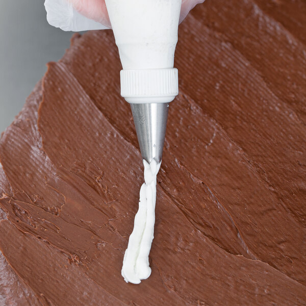 A person using an Ateco drop flower piping tip to frost a chocolate cake.