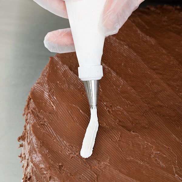 A person's hand using an Ateco open star piping tip to frost a cake.