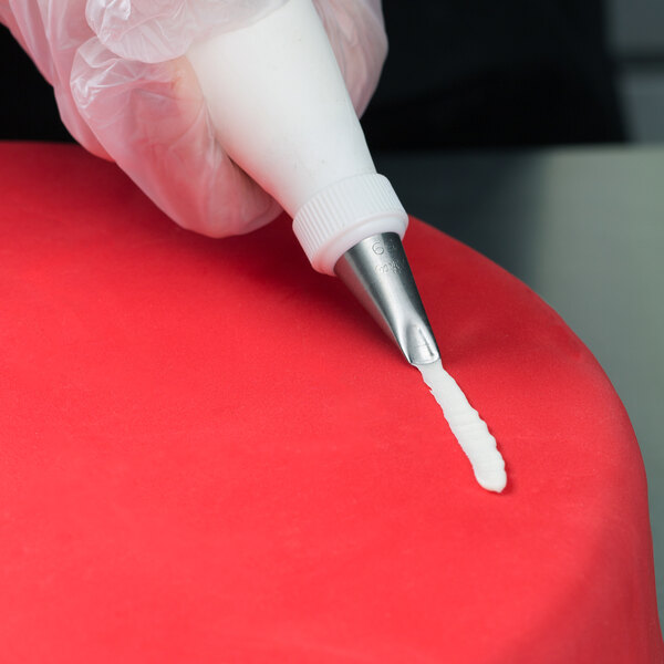 A hand using an Ateco curved petal piping tip over a red surface.