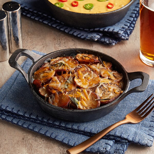A Valor pre-seasoned cast iron round casserole dish filled with cheesy potatoes next to a glass of beer on a table.