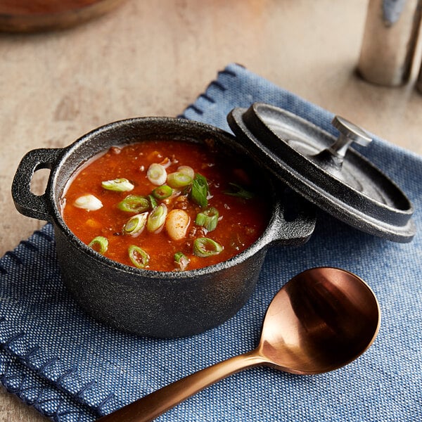 A Valor mini cast iron pot of soup with a lid and a spoon.