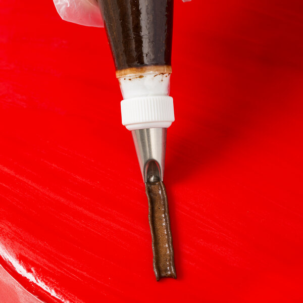 A hand using an Ateco Lily-of-the-Valley piping tip to pipe liquid onto a red surface.