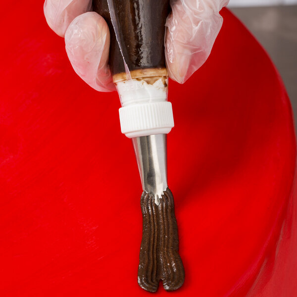 A hand using an Ateco leaf piping tip to pipe brown chocolate icing.