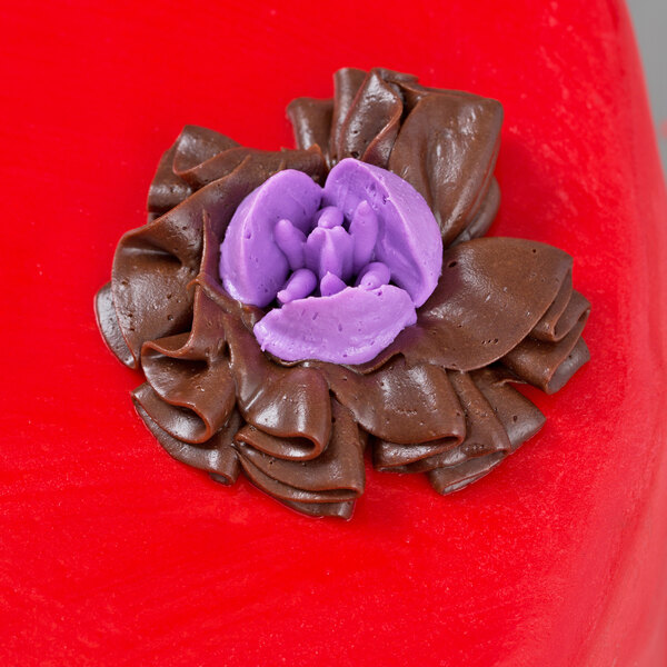 A close up of a chocolate cake with purple flowers piped on top using an Ateco Russian piping tip.