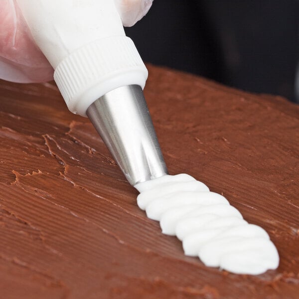 A person using an Ateco ruffle piping tip to pipe white frosting onto a cake.