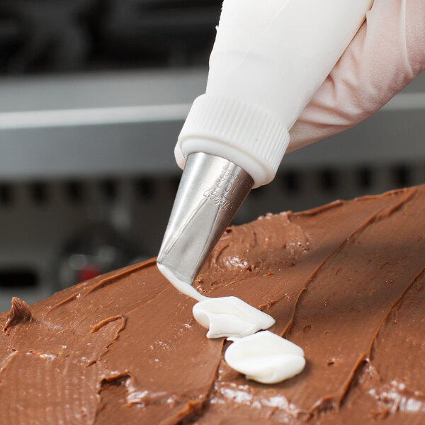 A hand using an Ateco rose piping tip on a pastry bag to frost a chocolate cake.