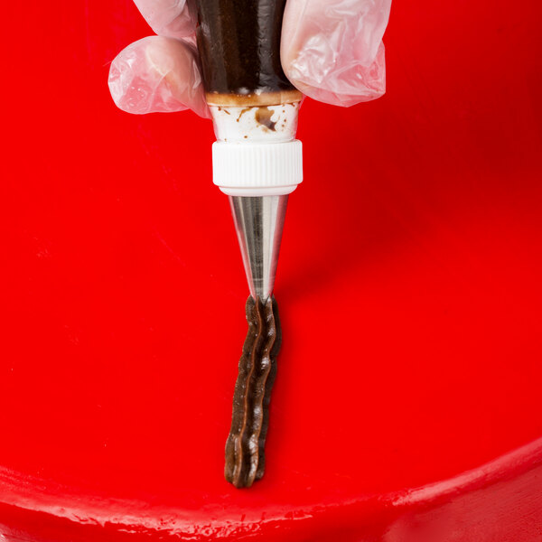 A hand using an Ateco open star piping tip to pipe chocolate icing onto a dessert.