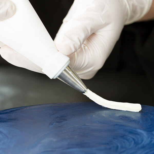 A person using an Ateco closed star piping tip to pipe blue frosting onto a cake.