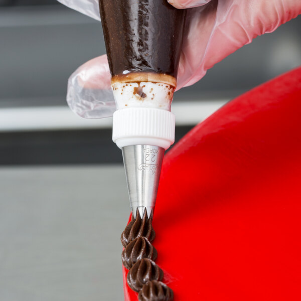 A person using an Ateco pastry bag with an open star piping tip to frost a chocolate cake.
