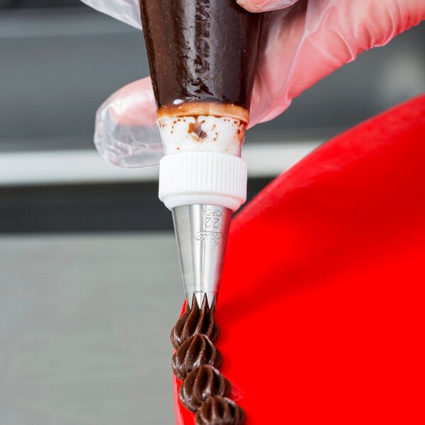 A person using an Ateco pastry bag with an open star piping tip to frost a chocolate cake.