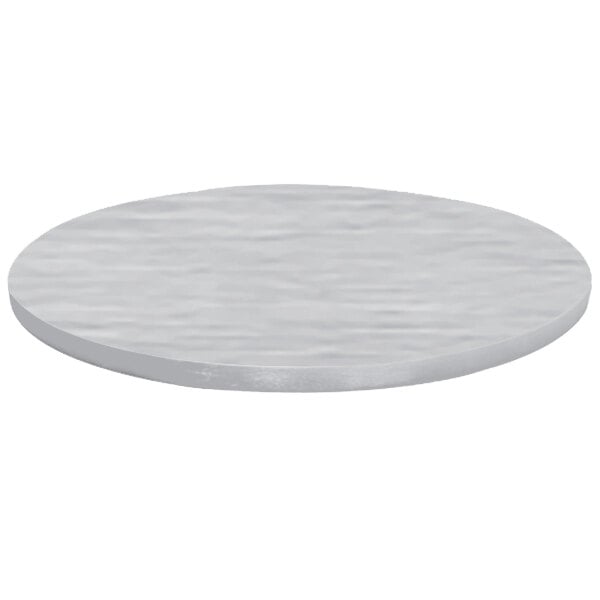 A close-up of a Tablecraft round translucent clear brushed aluminum table cover on a round table with a white surface.