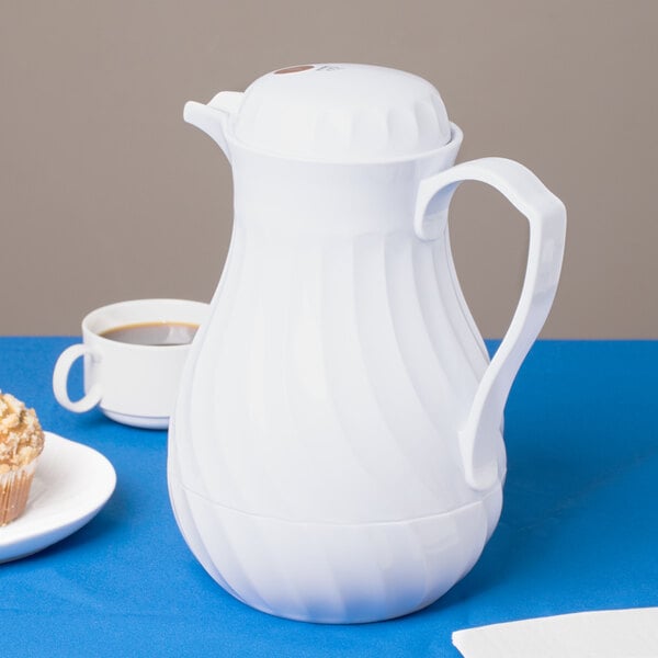 A white Vollrath SwirlServe beverage server on a blue table with a cup of coffee.