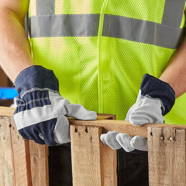 A person wearing Cordova denim work gloves and a safety vest holding a piece of wood.