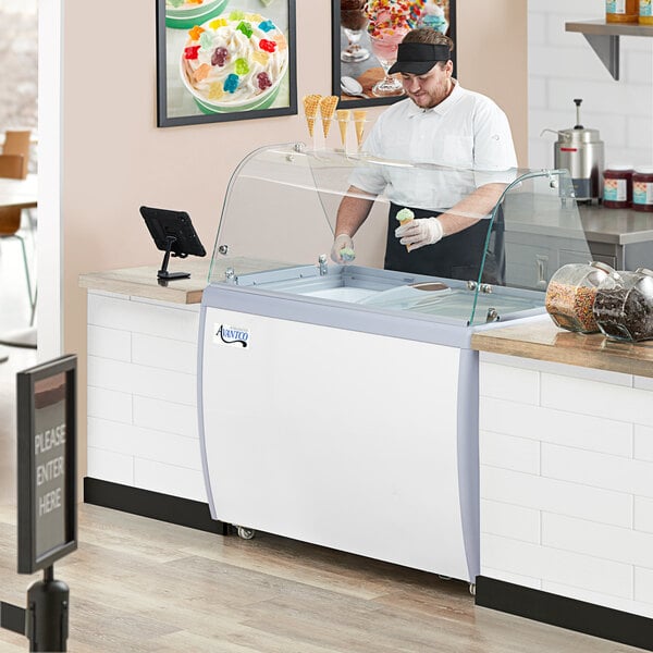 An Avantco ice cream dipping cabinet with a curved sneeze guard on a hospital cafeteria counter.