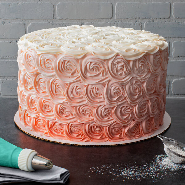 A frosted cake decorated with roses on a 14" white corrugated cake circle.