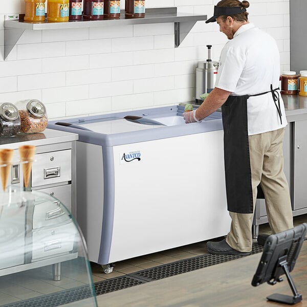 A man in a white apron standing in front of an Avantco ice cream dipping cabinet on a counter.