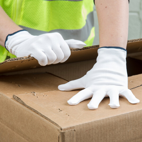 A person wearing a safety vest and Cordova medium weight white nylon work gloves putting on a cardboard box.