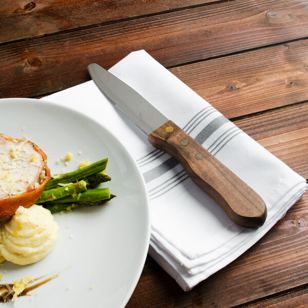 A white plate with a Walco stainless steel steak knife on it next to food.