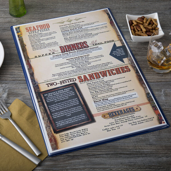 A dark blue Menu Solutions menu board on a table with a bowl of nuts and a glass of green liquid.