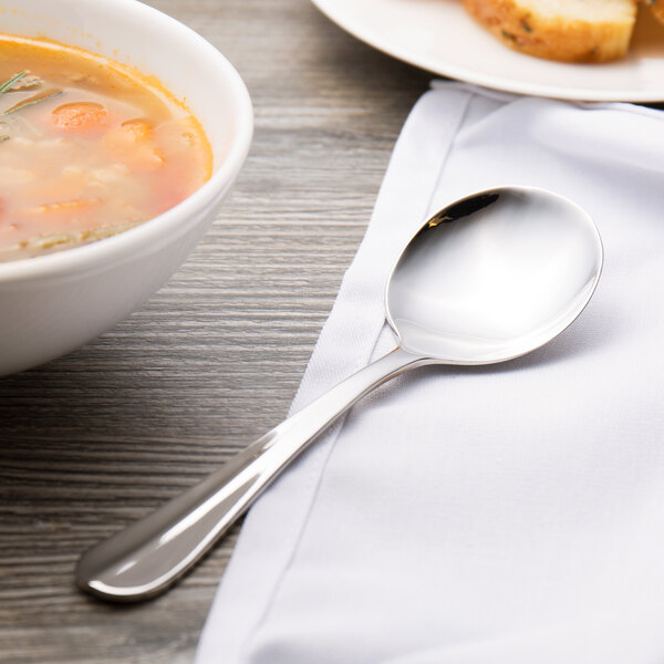A Walco Lancer stainless steel bouillon spoon in a bowl of soup on a table.