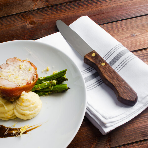 A plate with a Walco stainless steel steak knife on it next to food.