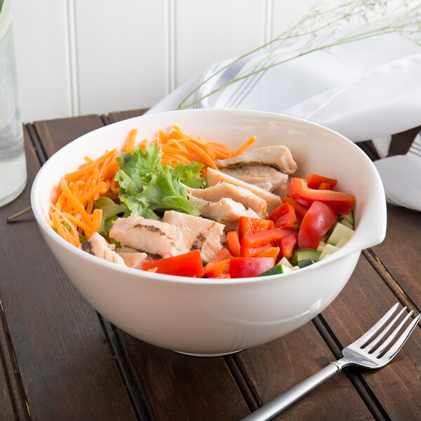 A close up of a Villeroy & Boch white porcelain salad bowl filled with chicken salad and vegetables with a fork on the table.