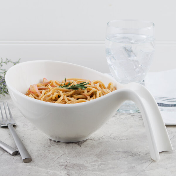 A Villeroy & Boch white porcelain handled bowl filled with pasta on a table with a glass of water.
