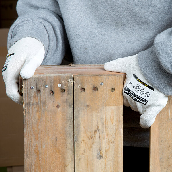A person wearing Cordova Monarch white engineered fiber cut resistant gloves with white polyurethane palm coating holding a piece of wood.