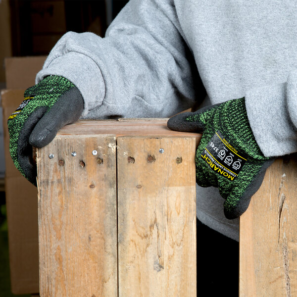 A person wearing Cordova Monarch Soft Green Engineered Fiber Cut Resistant gloves holding a piece of wood.