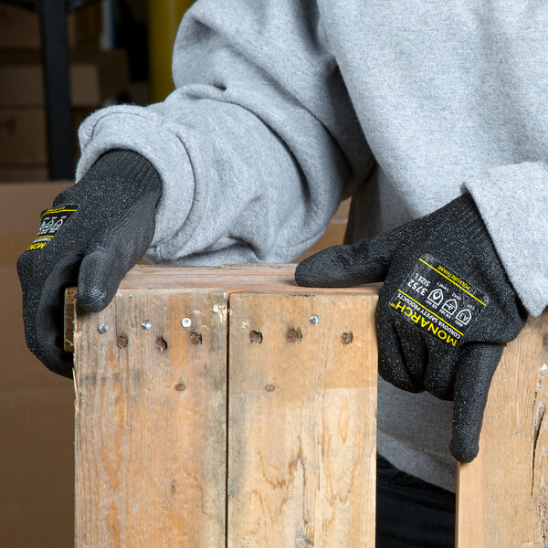 A person wearing Cordova Monarch black cut resistant gloves with black polyurethane palm coating holding a piece of wood.