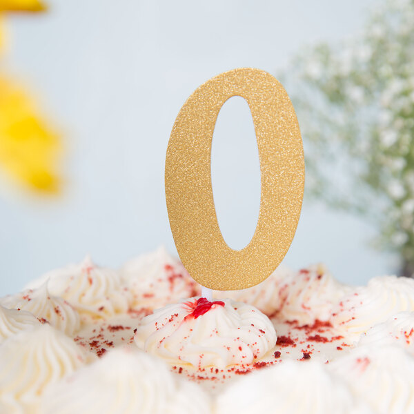 A white frosted cake with a gold glittery "0" on top.