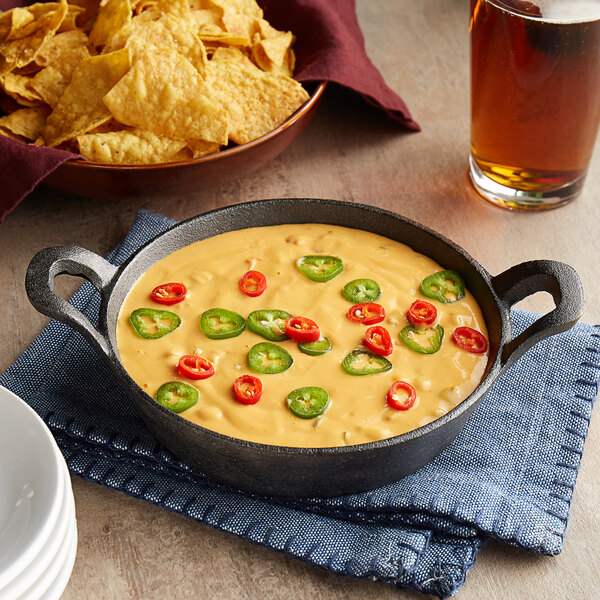 A Valor mini cast iron casserole dish with chili cheese dip and tortilla chips on a table.
