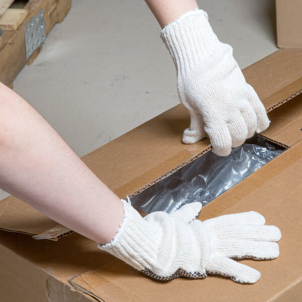 A person wearing Cordova medium weight work gloves with black PVC dots opening a box.