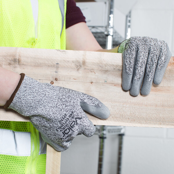 A person wearing Cordova Valor safety gloves with gray palm coating holding a piece of wood.
