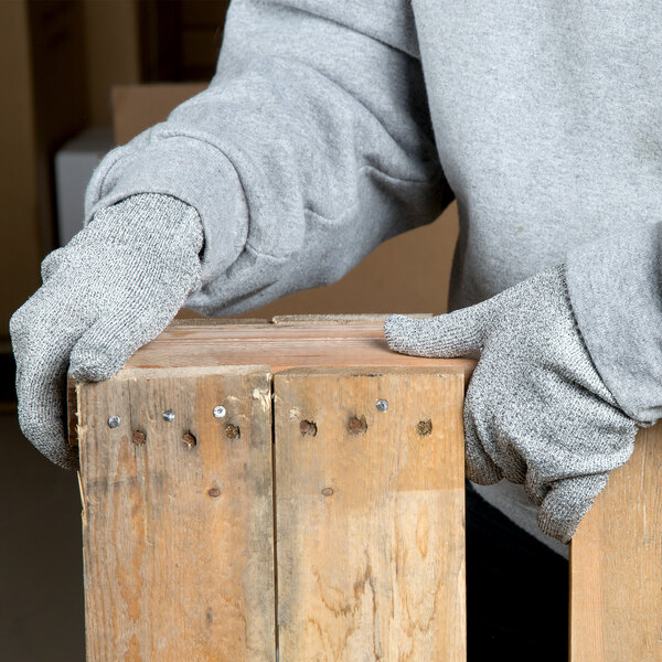 A person wearing Cordova Monarch gray engineered fiber cut resistant gloves holding a piece of wood.