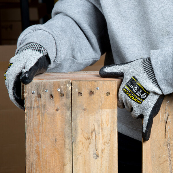 A person wearing Cordova Monarch gray heavy duty work gloves with black palm coating and holding a piece of wood.